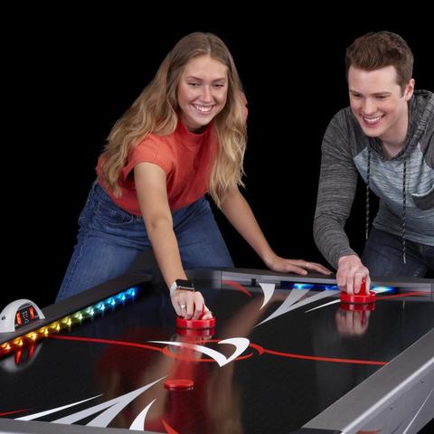 2 adults playing a game in the Fat Cat Volt LED Light-Up Air Hockey Table